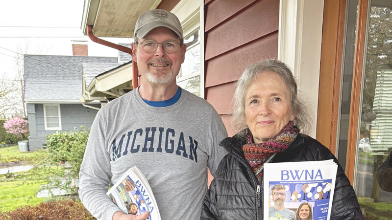 John Sandie and Georgina Head on a front porch with stacks of BWNA newsletters