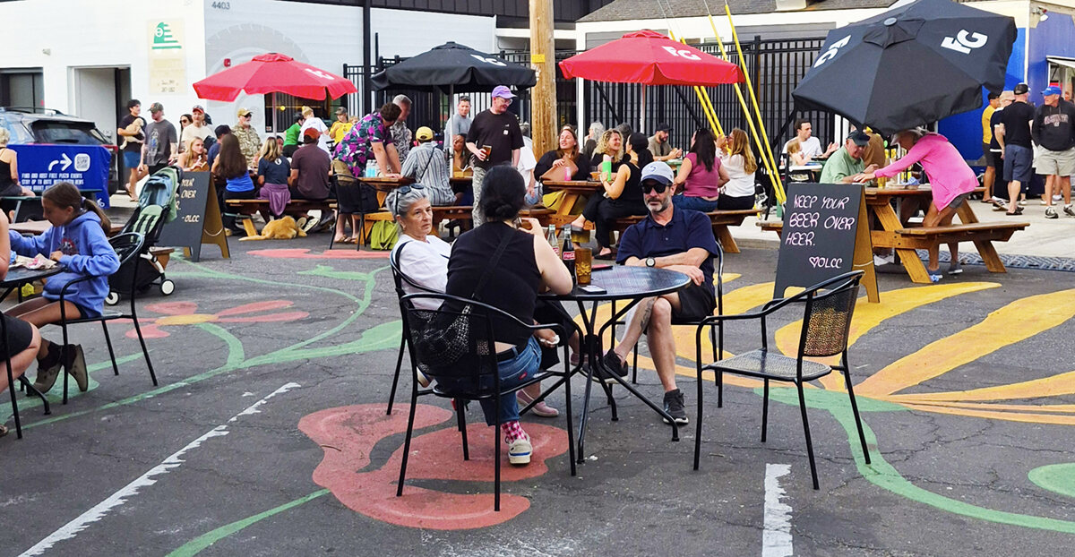 Neighbors at tables and umbrellas on the painted street surface at Beaumont Crossing
