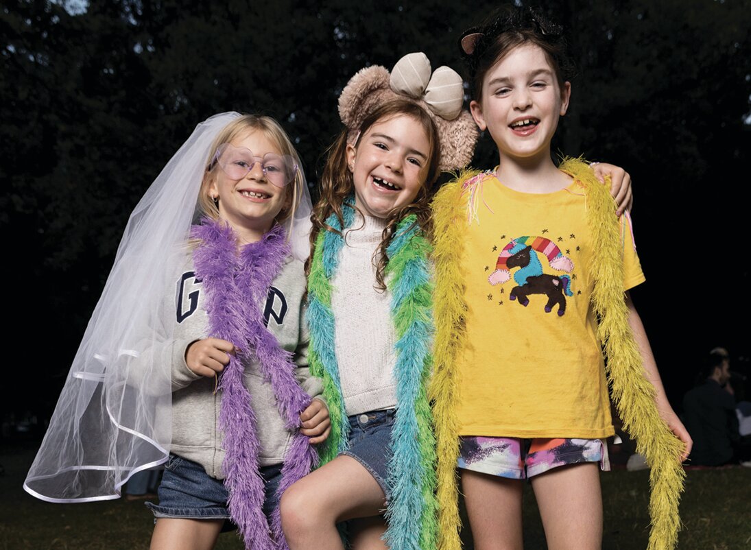 Three girls in feather boas and costume props pose at the block party photo booth.